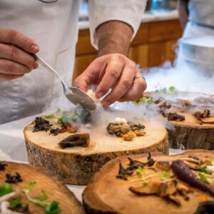 A chef artfully plating a gourmet dish with mushrooms and greens on wood slices.