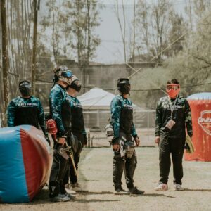 Group of men in paintball gear planning next moves in an outdoor field.